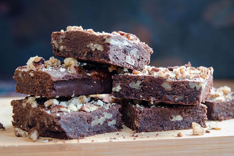 Ein Stapel Schokoladen-Pekannuss-Brownies, bestreut mit Pekannusskrümeln und zerstoßenen Walnüssen, frisch aus dem Ofen